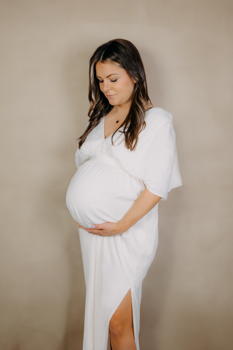 Schwangere Frau im weißen Kleid beim Babybauchshooting.